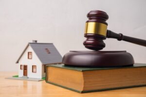 A small wooden house next to a green book with a gavel on top of it