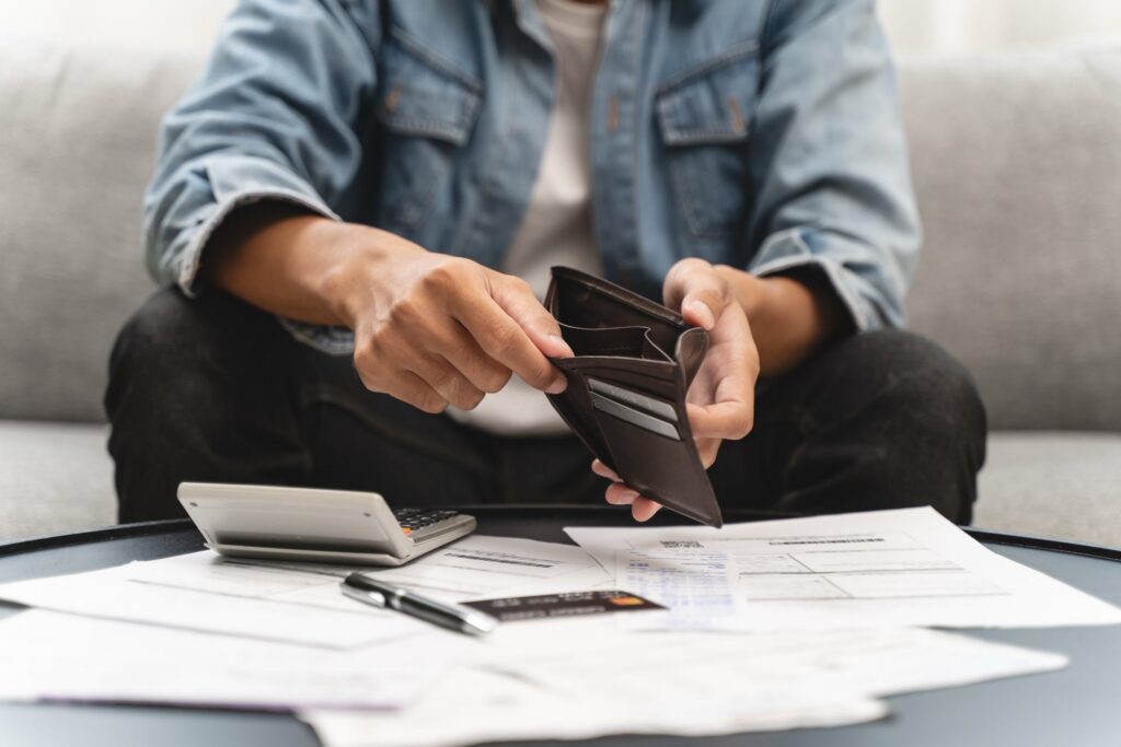 Person sitting on couch holding a wallet in front of a bunch of paperwork and calculator on the table