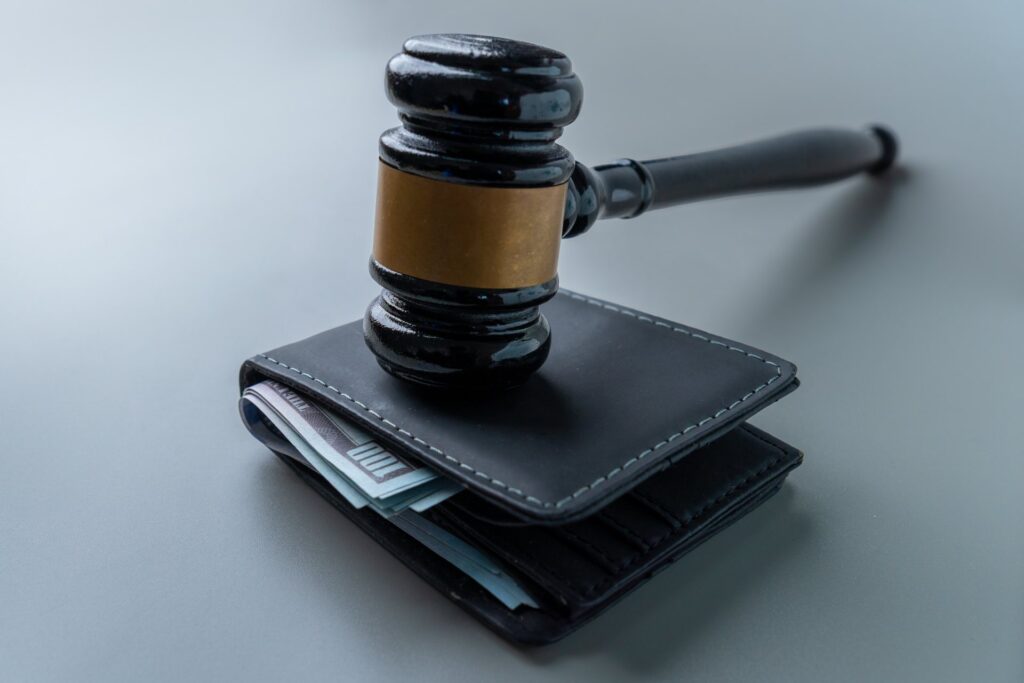 A judges gavel on top of a black wallet with money coming out of it