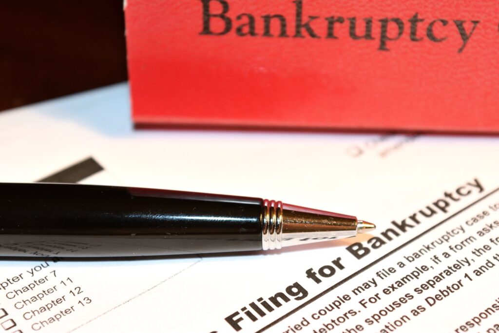 Red piece of paper that says bankruptcy next to a pen and paper with bankruptcy info on it