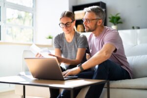 A man and woman sit on a couch in front of a laptop.