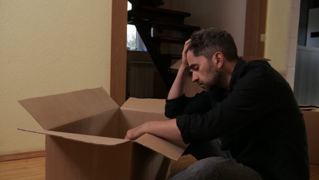 Man sitting in front of a moving box with his head in his hand
