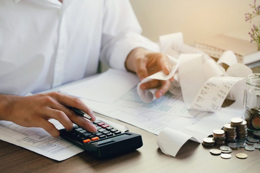 A person sitting at a desk holding receipts and on a calculator